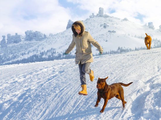 dog friendly ski resorts. Woman running down mountain trail with dogs.
