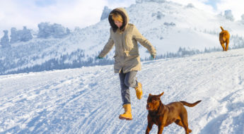 dog friendly ski resorts. Woman running down mountain trail with dogs.